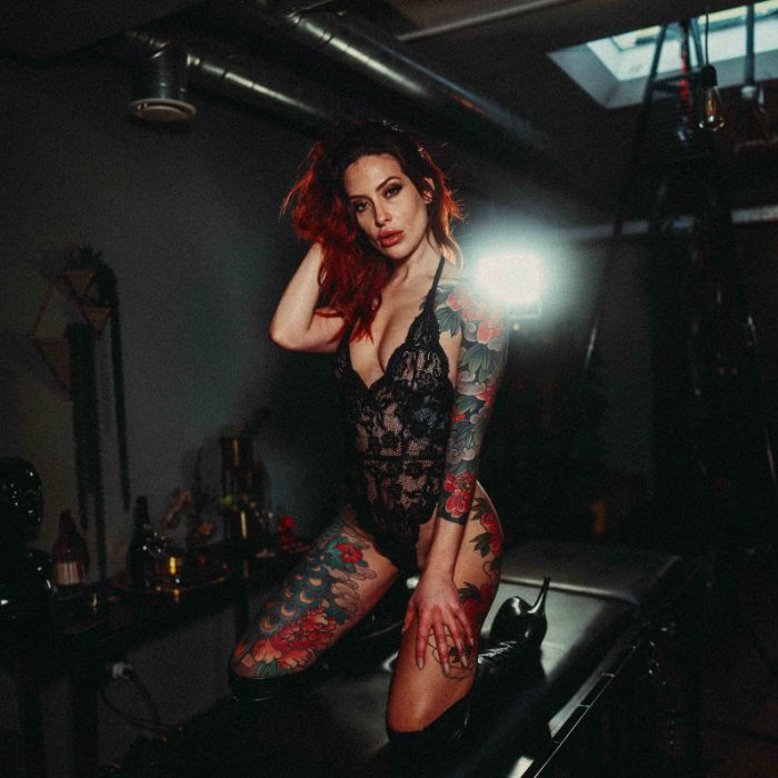 Mistress Adreena kneeling on a table in lingerie.