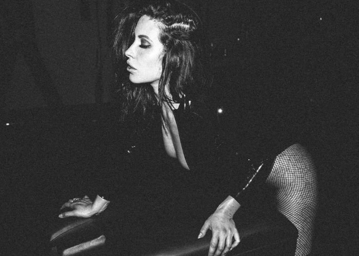 Mistress Adreena in black and white, leaning on a table 