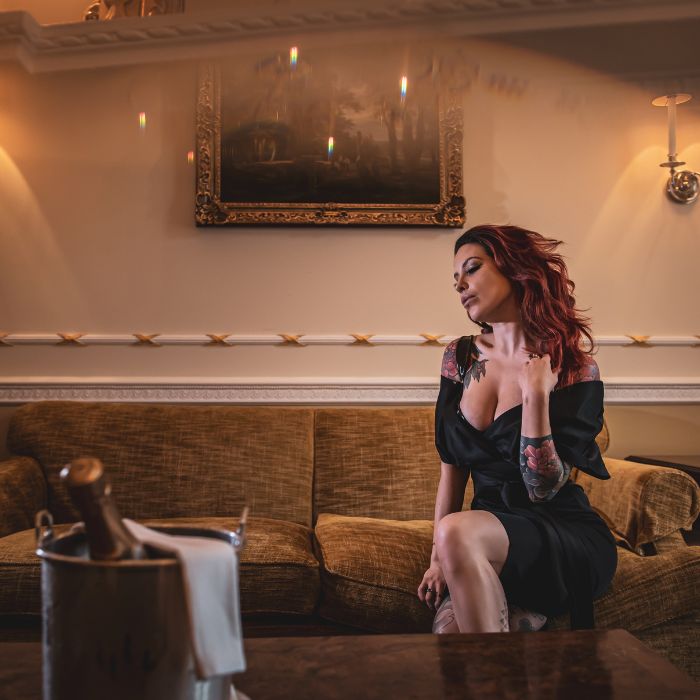 Mistress Adreena sitting on a sofa in a luxurious room.