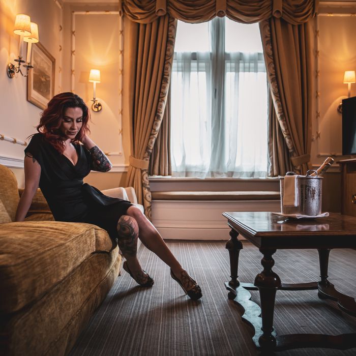 Mistress Adreena sitting on a sofa in a luxurious room.