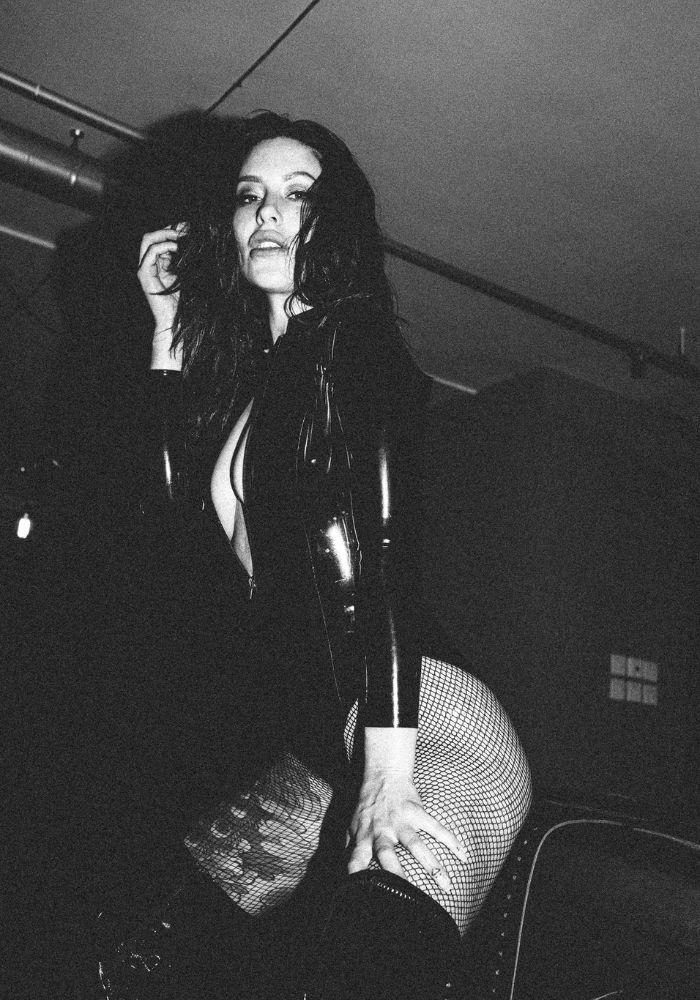 Mistress Adreena in fishnets and latex looking directly at you.