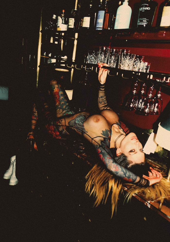 Mistress Adreena in a mesh outfit, layed across a bar.
