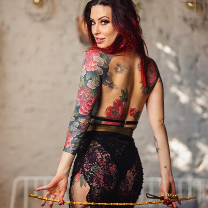 Mistress Adreena in black lingerie holding a rattan cane below her ass. 