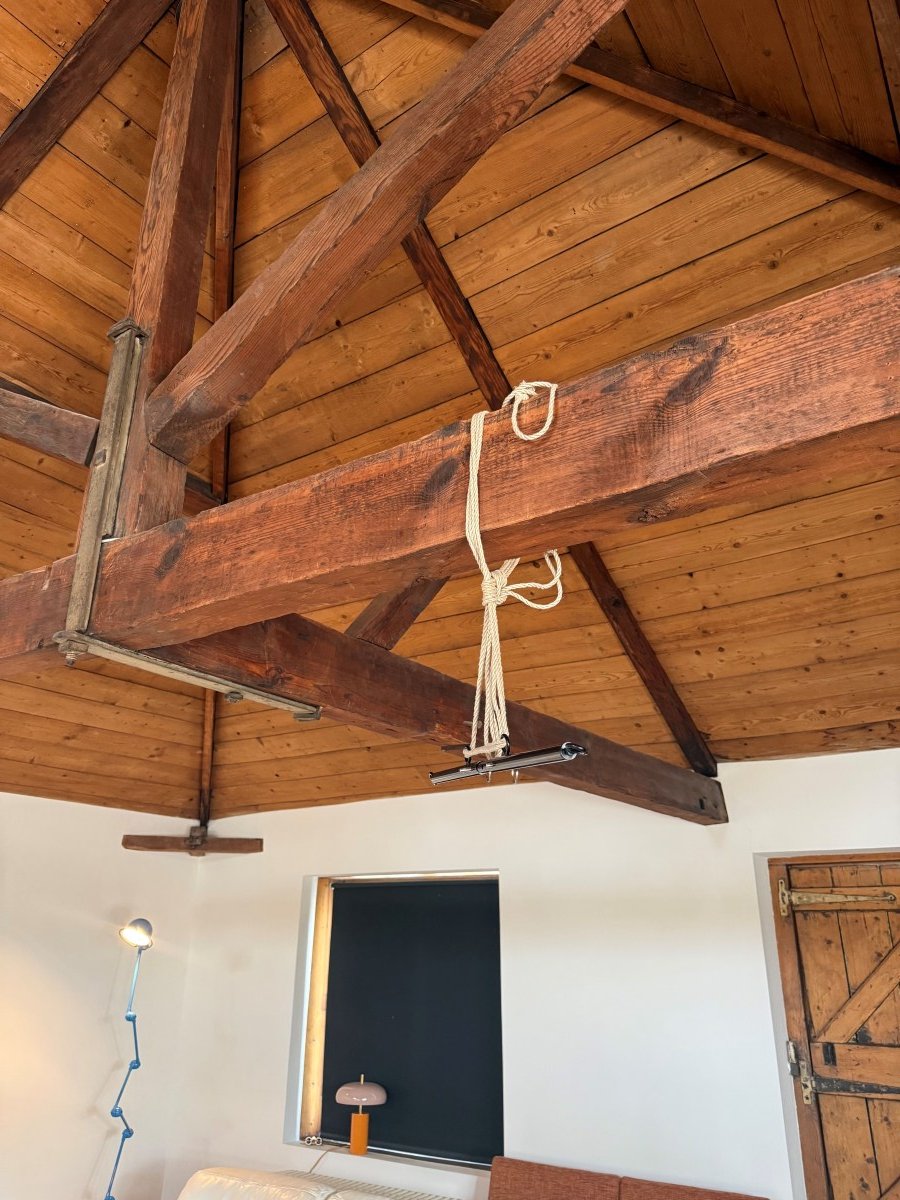 Ceiling with wooden beams, a hanging rope fixture, and part of a room with a couch and window.