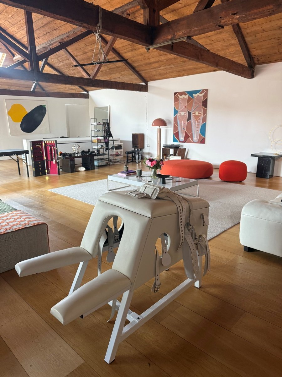 Spacious loft with wood beams, white leather furniture, red seating, and a beige padded apparatus with straps.